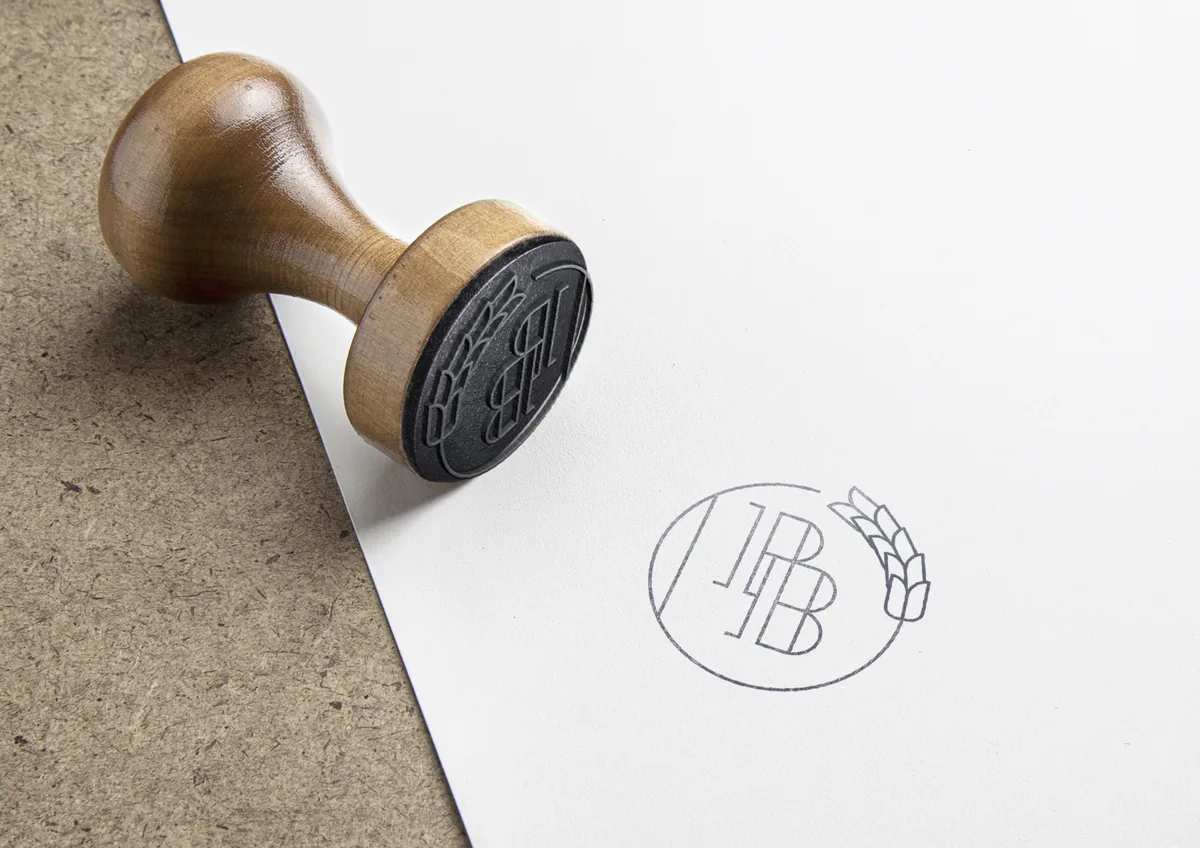 A wooden hand stamp printing the round Palma Bread monogram onto paper